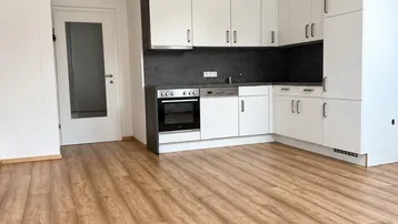 Moderne Einbauküche mit weißen Schränken und dunkler Arbeitsplatte in einem hellen Raum.