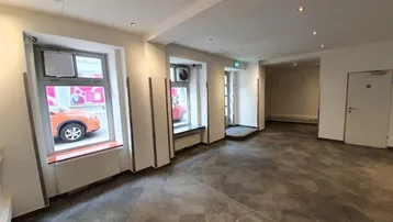 Geräumiger, leerer Geschäftsraum mit großen Fenstern zur Straße und modernem Fliesenboden.