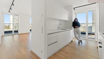 Helle, moderne Küche mit weißen Schränken und Holzboden, offen zum Wohnbereich mit Balkonzugang.