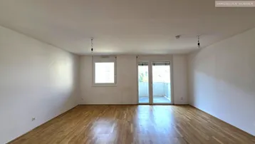 Helles Zimmer mit Parkettboden und Zugang zu einem Balkon, ideal als Wohn- oder Schlafbereich.