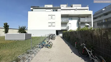 Moderne Wohnanlage mit Fahrradabstellplätzen und gepflegter Außenanlage unter blauem Himmel.