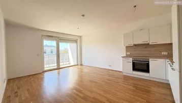 Heller Wohnbereich mit offener Küche, Parkettboden und Zugang zum Balkon.