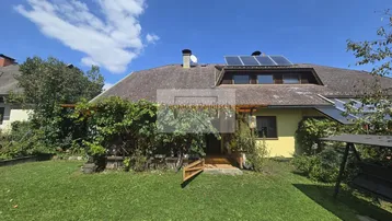 Großer Garten mit grüner Rasenfläche, überdachtem Sitzbereich und Solaranlage auf dem Dach.