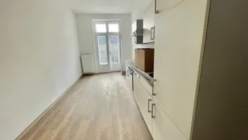 Lange Küche mit Einbauschränken, Laminatboden und Zugang zu einem Außenbereich.