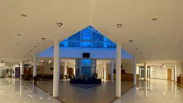 Geräumige und helle Lobby mit hoher Decke, Glasdach und dekorativem Fliesenboden in einem modernen Gebäude.