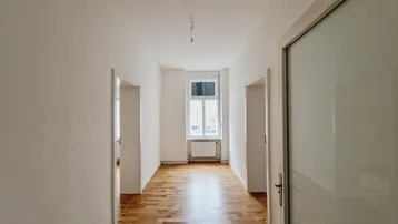 Heller Flur mit Holzboden und weißen Wänden, der zu weiteren Räumen führt und Tageslicht bietet.