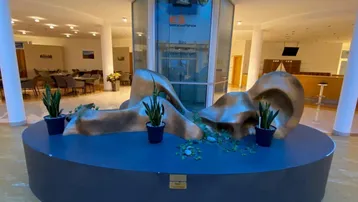 Geräumige Lobby mit moderner Skulptur, Glasaufzug und Sitzbereichen im Hintergrund.