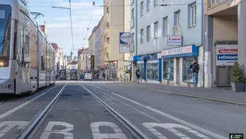 Eine belebte Stadtstraße mit einer Straßenbahn und Geschäftsgebäuden unter blauem Himmel.