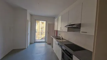 Helle Küche mit weißen Schränken, Einbaugeräten und Zugang zu einem kleinen Balkon.