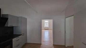 Moderne Küche mit grauen Schränken, dunkler Arbeitsplatte und Blick in einen weiteren Raum.