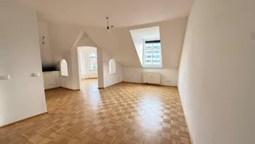 Geräumiger Wohnbereich im Dachgeschoss mit Parkettboden und schrägen Wänden, der viel Potenzial bietet.