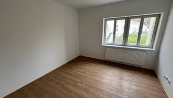 Heller Raum mit Laminatboden und großem Fenster, ideal als Schlaf- oder Arbeitszimmer.