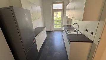 Helle Küche mit weißen Schränken, dunkler Arbeitsplatte und großem Kühlschrank.