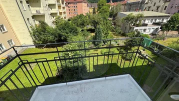 Balkon mit Blick auf einen grünen Innenhof und die umliegende Berglandschaft.