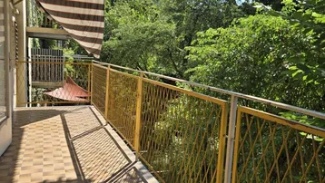 Langer, sonniger Balkon mit Fliesenboden, gelbem Geländer und Blick ins Grüne.
