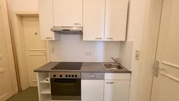 Kompakte Einbauküche mit weißen Schränken, Herd, Backofen und integriertem Geschirrspüler.