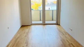 Helles Zimmer mit Parkettboden und Zugang zu einem Balkon, ideal als Wohn- oder Schlafbereich.