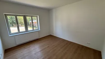 Leeres Schlafzimmer mit Laminatboden, großem Fenster und Heizkörper, bereit zur individuellen Gestaltung.