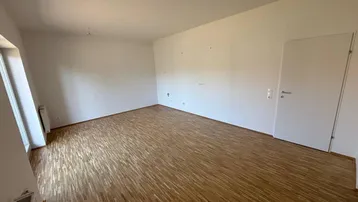 Helles, leeres Zimmer mit Parkettboden und weiß gestrichenen Wänden, bereit zur individuellen Gestaltung.
