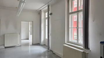 Geräumiger, heller Raum mit großen Fenstern, Heizkörpern und funktionaler Beleuchtung, ideal als Bürofläche.