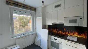 Moderne Küche mit weißen Schränken, dunkler Arbeitsplatte und einem Fenster mit Blick ins Grüne.