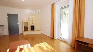 Helles Wohnzimmer mit Parkettboden, Kamin und Zugang zum Balkon.