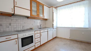 Funktionale Küche mit weißen Schränken, Fliesenrückwand und Fenster.