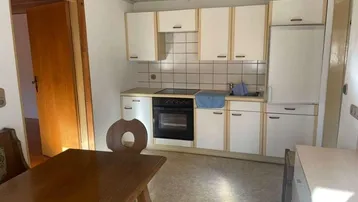 Funktionale Küche mit weißen Schränken, integriertem Backofen und einem rustikalen Holztisch.