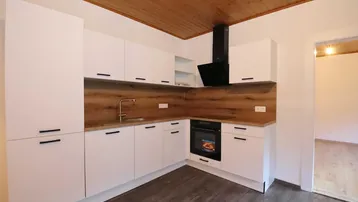 Moderne Einbauküche mit weißen Schränken, Holzarbeitsplatte und Holzdecke, ausgestattet mit Backofen und Dunstabzugshaube.