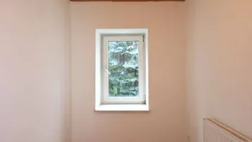 Kleiner, heller Raum mit Holzdecke, Parkettboden und einem Fenster zur Natur.