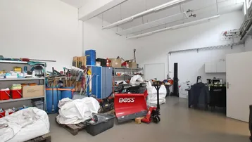 Großer Lagerraum mit hohen Decken, gefliestem Boden und verschiedenen Geräten und Regalen.