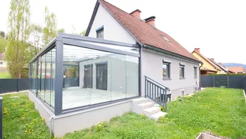 Modernes Haus mit großem Wintergarten und angrenzendem Rasenbereich, ideal für Entspannung.