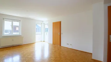 Helles, leeres Zimmer mit Parkettboden und Zugang zu einem Balkon oder einer Terrasse.