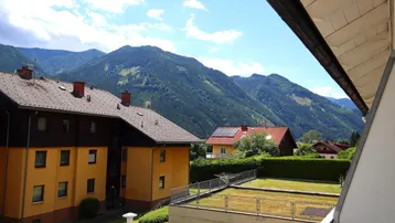 Weitläufiger Blick vom Balkon auf die grüne Berglandschaft und benachbarte Gebäude.