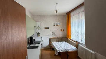 Gemütliche Küche mit heller Einbauküche, Essbereich und Holzfußboden, gut beleuchtet durch das Fenster.