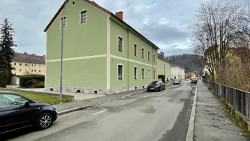 Gebäude mit hellgrüner Fassade an einer Straße unter bewölktem Himmel.