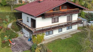 Traditionelles Haus mit rotem Ziegeldach, umlaufenden Holzbalkonen und großem Garten in Hanglage.