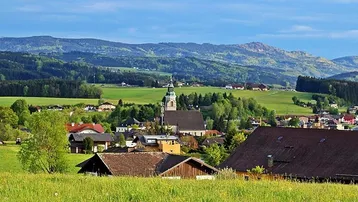 Malerische Weitblickaufnahme eines charmanten Dorfes mit Kirche, umgeben von grünen Hügeln und Feldern.