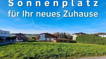 Sonniges Grundstück in ländlicher Umgebung mit Blick auf grüne Hügel und moderne Wohnhäuser.