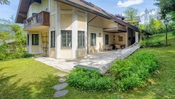 Traditionelles Haus mit großem Garten und gepflasterter Terrasse, umgeben von viel Grün.