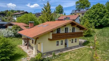 Traditionelles Haus im alpenländischen Stil mit Ziegeldach und Balkon, umgeben von viel Grün.