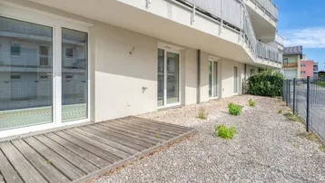 Erdgeschoss-Terrasse mit Holzdeck und Kiesfläche vor einem modernen Mehrfamilienhaus.