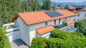 Luftaufnahme eines Wohnhauses mit Ziegeldach, Solaranlage und Bergblick, umgeben von viel Grün.