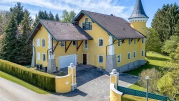 Charmantes Anwesen mit gelber Fassade, Turm und gepflegter Auffahrt, umgeben von viel Grün.