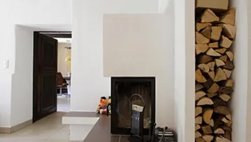 Moderner Kamin mit integriertem Holzregal und Fliesenboden in einem Wohnbereich.