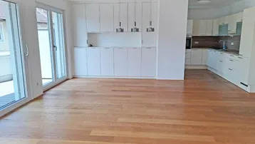 Helles, offenes Wohnzimmer mit integrierter Küche, Holzboden und Zugang zu einer Terrasse.