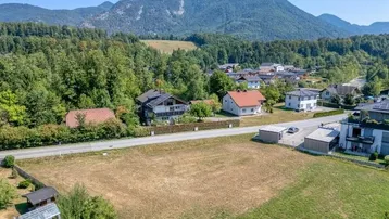 Luftaufnahme eines Grundstücks mit umliegenden Häusern, viel Grün und beeindruckender Bergkulisse.