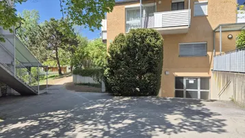 Mehrfamilienhaus mit Balkonen, Außenparkplätzen und begrüntem Umfeld an einem sonnigen Tag.