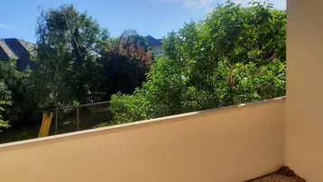 Blick von der Loggia ins Grüne mit Bäumen und einem Spielplatz im Hintergrund.