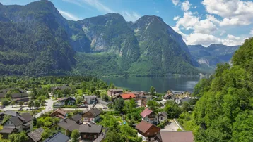 Panoramablick auf ein malerisches Dorf am Seeufer, umgeben von majestätischen Bergen und grüner Natur.